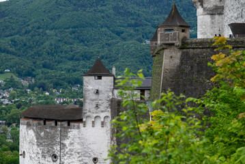 Stone fortress walls and turrets framed by spring greenery with mountainside village in the distance. © Andrei Tomas