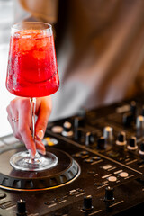 A person holds a stemware glass filled with a vibrant red alcoholic cocktail and ice over a...