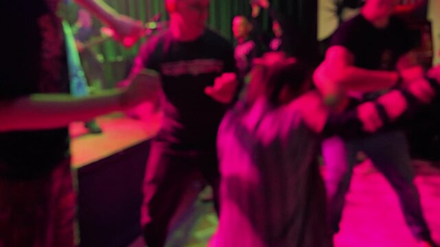 People dancing with motion blur in dark nightclub. Energetic punk rock show creates lively, chaotic atmosphere. Vibrant blue and magenta lights illuminate dance floor and stage