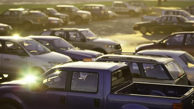 Packed retail parking under late golden light tight rows of vehicles, bustling arrival scene, overlapping shadows and close proximity spaces, commercial hub
