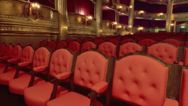 Wide auditorium view with red seats and gilded balconies, soft stage lighting casts cinematic warm glow, empty house moments before premiere, opulent decor