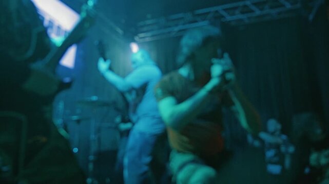 An energetic rock band performs on a dark stage. The video is out of focus. A chaotic, powerful atmosphere. The original concept of the underground music scene
