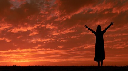 Fototapeta premium A silhouette of a mature woman stands with arms raised at sunrise, symbolizing transformation and new beginnings in life.