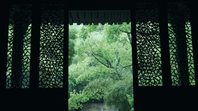 View of lush green trees through traditional Chinese carved lattice window frame in a garden