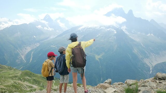 Mother with two kids pointing at a stunning mountain peak during a summer hike, enjoying the alpine landscape and sharing a moment of discovery and togetherness