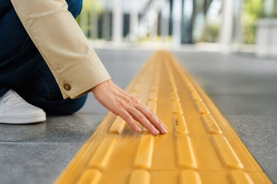 Hand touching tactile paving on a sidewalk with yellow guidance strip for accessibility and safe navigation
