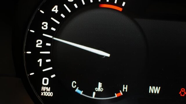 Close-up view of a modern car's dashboard tachometer with the needle moving, indicating engine RPM and temperature, showcasing vehicle performance and operational status.