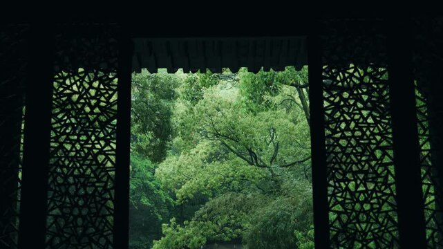 Traditional Chinese carved lattice window framing a view of lush green forest trees