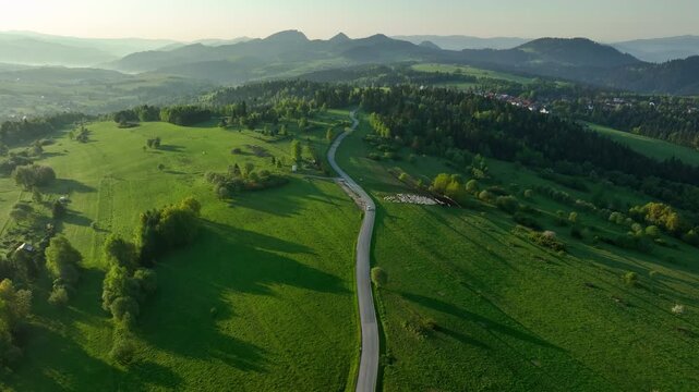 Cinematic drone shot of countryside road stretching towards Pieniny mountains at sunrise, spring meadows in Czorsztyn