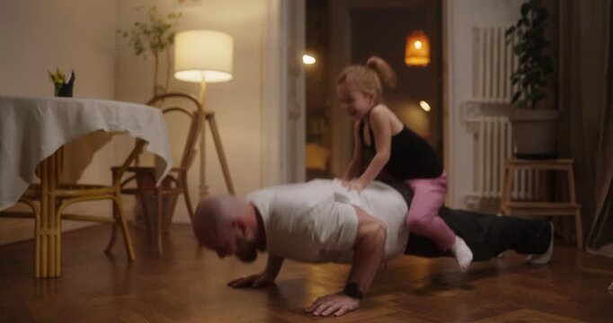A dad joyfully exercises while his daughter playfully rides on his back during push-ups, creating a warm family moment