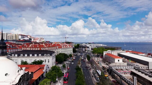 stablishing shot of Time Out Market and the Lisbon waterfront in Portugal featuring historic architecture, city traffic, tram lines, and panoramic views toward the Tagus River under dramatic clouds.