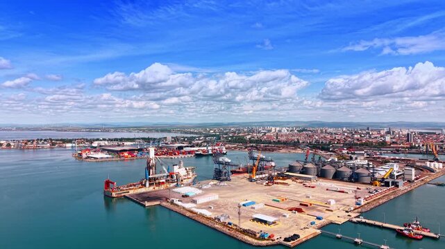 Approaching a huge port and vast cityscape of the modern city. Commercial maritime facility against blue sky with fluffy cloudscape. Aerial view.