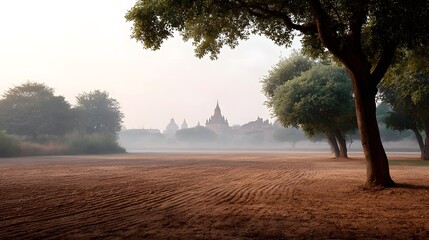 Naklejka premium Misty forest trees frame a distant ancient religious structure in a serene atmospheric landscape