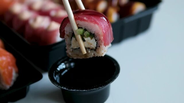 Assorted sushi sets in black plastic trays with tuna rolls topped with Japanese mayo, eaten with wooden chopsticks and soy sauce dipping