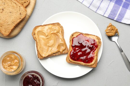 Tasty sandwiches with peanut butter and jam on grey table, flat lay