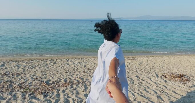 Smiling woman leading partner on sunlit beach for authentic moment