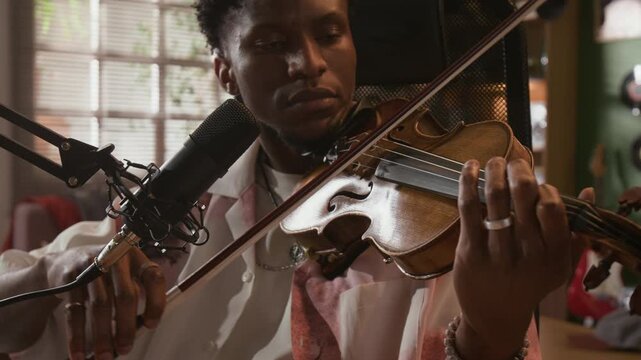 Close up shot of young adult African American male music producer recording violin performance in home studio for sound production, sampling