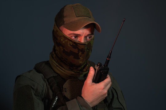 Private military contractor wearing a camouflage balaclava mask and holding a radio transmitter, special forces commando radio operator concept