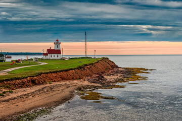Wood Islands Lighthouse on the south coast of Prince Edward Island, Canada, above red cliffs and shoreline at dusk. © Robert