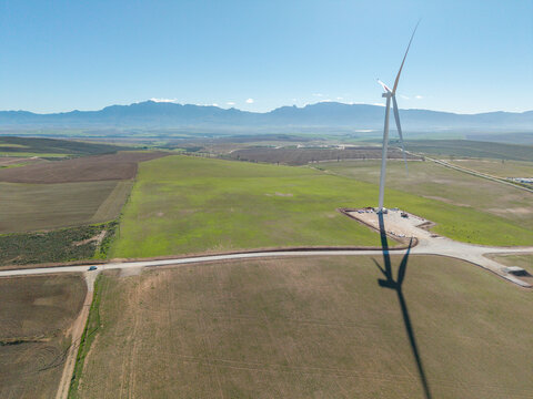 Aerial view of a large wind turbine standing in green agricultural fields with mountains in the background Swellendam, Western Cape, South Africa.