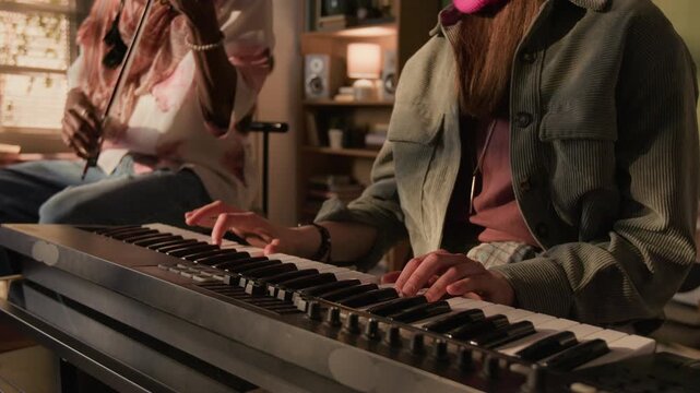 Cropped shot of young adult female musician playing electronic synth keys while performing in duo with Black male violinist during home based rehearsal