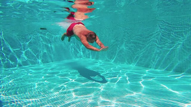 Man Dives and Swims Underwater in Vibrant Blue Pool Water