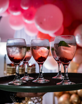 Copas con c&oacute;cteles rosados sobre bandeja en celebraci&oacute;n elegante con globos decorativos