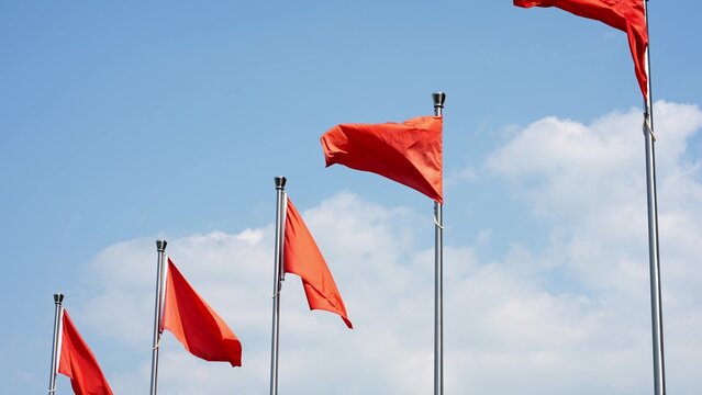 Five red flags waving in the wind against a blue sky with white clouds