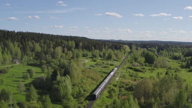 Tracking aerial shot of Ruskeala Express train going through the surroundings of Sortavala on sunny summer day. Karelia, Russia.