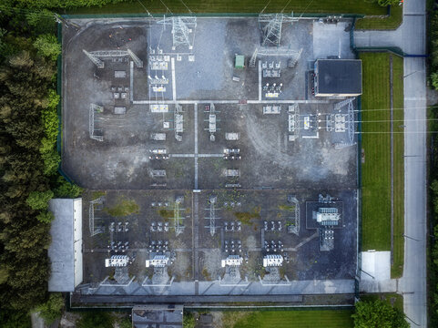 Aerial view of an electrical substation with transformers and power lines surrounded by lush green trees in Drogheda, County Louth, Ireland.