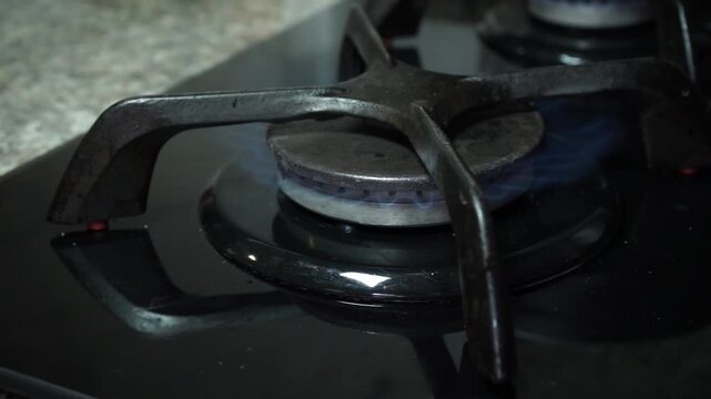 Close up side view of a kitchen gas stove burner igniting with a blue flame