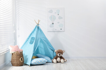 Wigwam, toy bear and pillows near white wall in child's room, space for text © New Africa