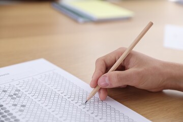 Student taking test at wooden desk in classroom, closeup