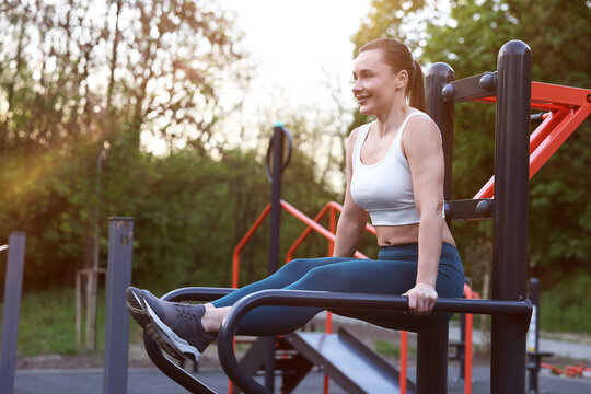 Athletic woman exercising on parallel bars at outdoor gym. Space for text
