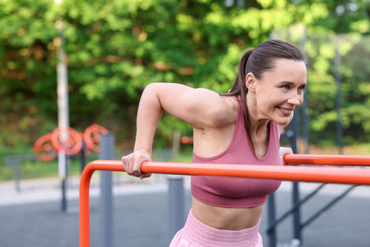 Athletic woman exercising on parallel bars at outdoor gym