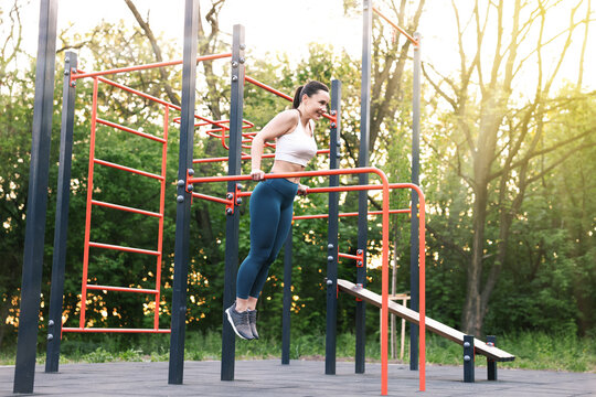 Athletic woman exercising on parallel bars at outdoor gym