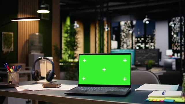 Chroma key on laptop in empty office interior with open space layout and professional design. Large windows reveal vibrant city skyline at night, corporate success and enterprise headquarters.