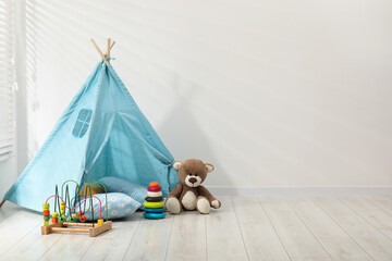 Wigwam, toys and pillows near white wall in child's room, space for text © New Africa