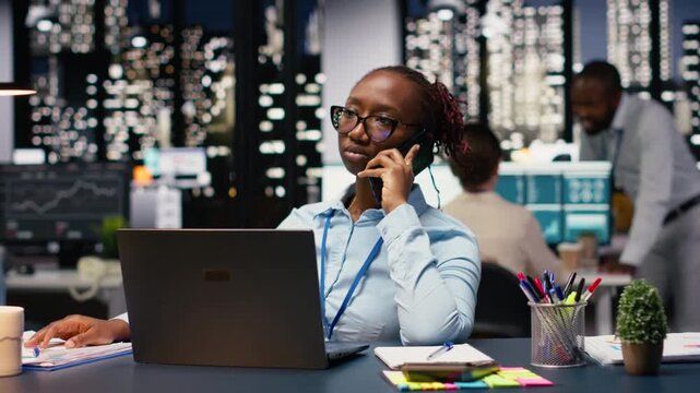 Businesswoman in office receiving call from client requesting assistance, using laptop. Entrepreneur talking over the phone with customer inquiring about commissioned project progress.