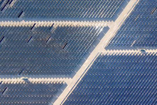 Aerial view of rows of blue solar panels in a geometric pattern across a desert landscape with sunlight reflections in Enterprise, Nevada, United States.