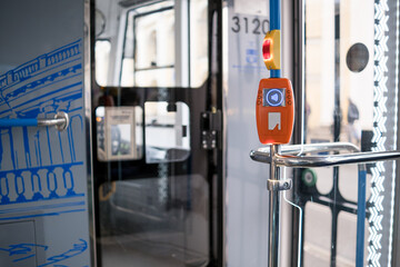 Interior of a public transport vehicle featuring a stop request button and door mechanism, with urban scenery visible through the windows
