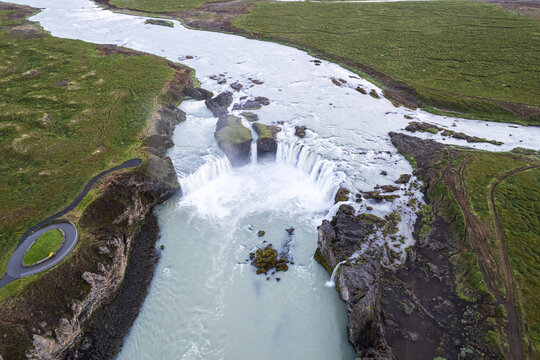 Aerial view of Godafoss Waterfall with cascading white water and rocky cliffs surrounded by green landscape Thingeyjarsveit, Iceland.