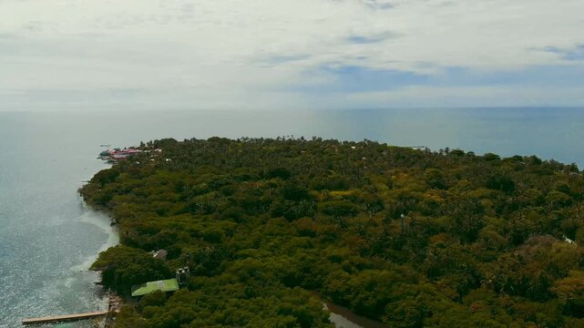 Lateral drone view of Mucura Island revealing dense jungle and minimal huts