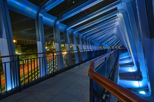 View of the modern JPO Pandanaran pedestrian bridge at night featuring geometric blue LED lighting and light trails from traffic below in Semarang, Central Java, Indonesia.