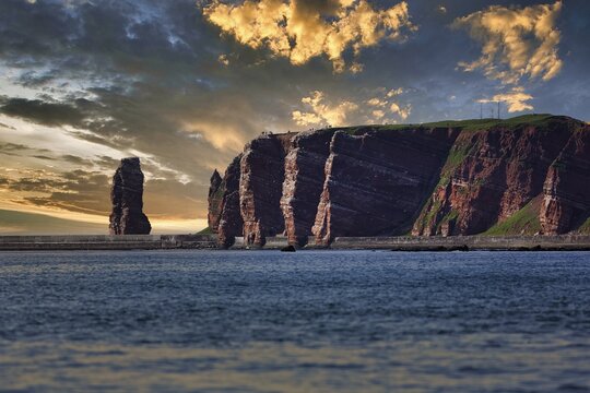 View from the sea to the rocky island of Helgoland with surf pillar Lange Anna, dramatic evening sky, North Sea, Schleswig-Holstein, Germany