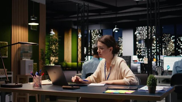 Woman employee looking over paperwork and data on laptop, preparing budget reports before deadline. Female consultant documenting company balance sheets and income statements at night.