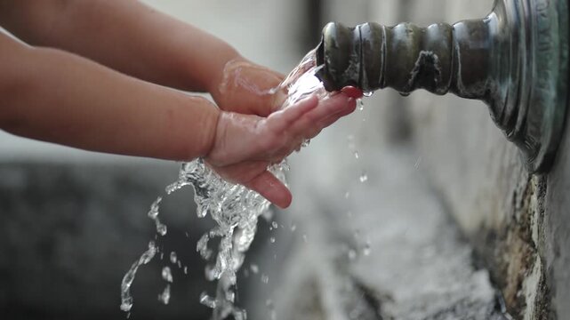 A child is washing their hands under a vintage faucet with flowing cold and clear water, slow motion isolated cinematic shot. The scene is peaceful and calming