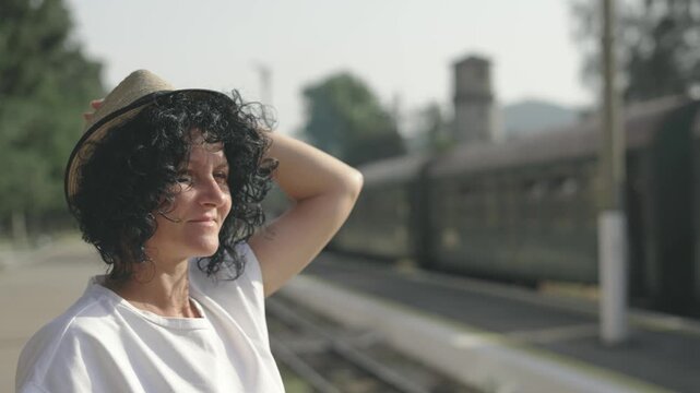 A woman wearing a hat and smiling at the camera standing on a train platform