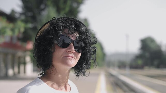 A woman wearing a hat and smiling at the camera standing on a train platform
