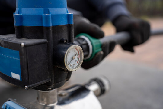 Hand in black work glove connecting an HDPE pipe with a plastic compression fitting to the automatic electronic pressure controller unit of an electric water booster pump.